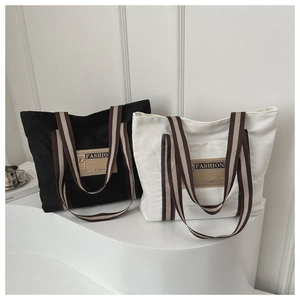 Dettaglio di borse tote in tela nere e beige con manici a righe su supporto geometrico