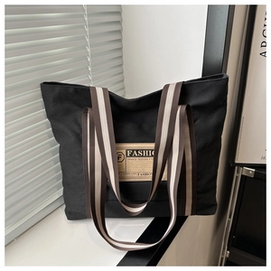 Dettaglio della borsa tote in tela nera con manici intrecciati a righe e patch moda