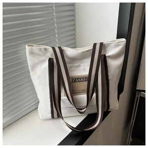 Dettaglio di borsa tote in tela bianca con toppa fashion e tracolla a righe