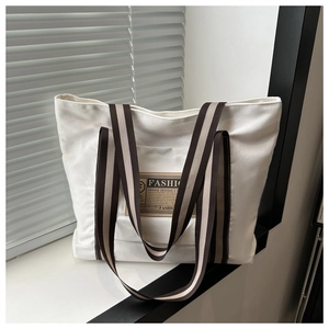 Dettaglio della grande borsa tote in tela con spallacci a righe ed etichetta