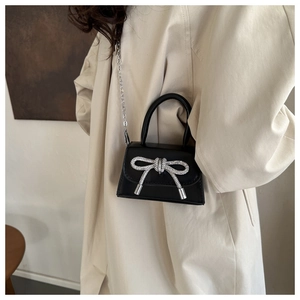 Detail of black patent leather mini bag with silver rhinestone bow and metal chain strap