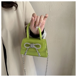 Close-up of mini green handbag with rhinestone bow and silver chain strap