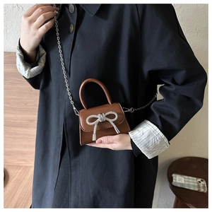 Close-up of mini brown leather handbag with sparkling rhinestone bow and silver chain strap