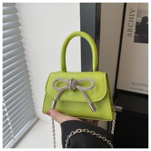 Close-up of grass green mini handbag with a sparkling rhinestone bow and silver chain