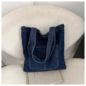 Detail of dark blue denim tote bag with yellow stitching and front pocket on minimalist chair