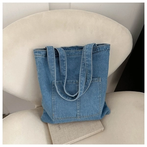Detail of blue denim tote bag with front pocket placed on a beige chair for daily style