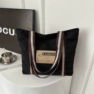 Grande borsa tote in tela nera con manici a righe su una scrivania minimalista