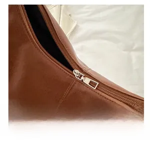 Macro detail of the smooth silver zipper and premium brown leather texture on shoulder bag