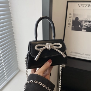 Mini black handbag with rhinestone bow and silver chain strap shown in lifestyle setting