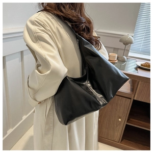 Detail of a soft black matte leather tote bag worn by a model in a beige coat