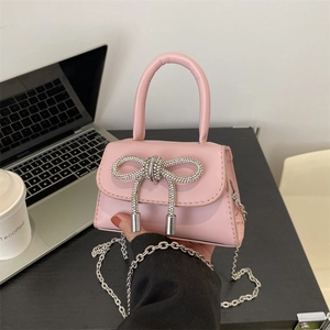 Pink mini crossbody bag with rhinestone bow and silver chain strap on a black desk