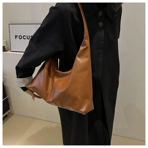 Detailed side view of large caramel brown leather shoulder bag on model in a modern room