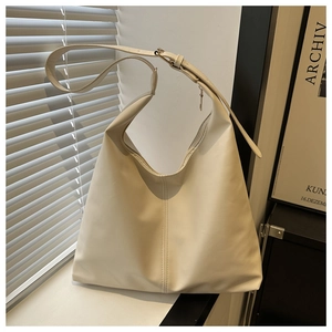 Detail of a creamy white leather hobo bag with vertical stitching on a white ledge