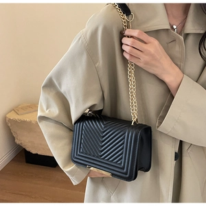 Detail of black quilted crossbody bag with chevron pattern and gold chain strap on model