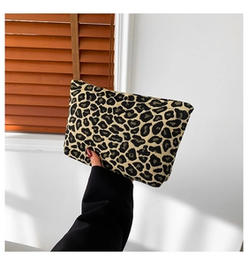 Detail of leopard print clutch bag in textured canvas held by a model in soft daylight