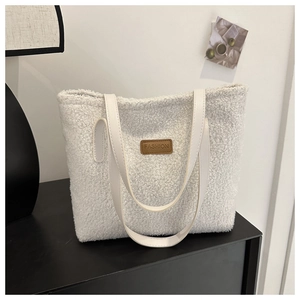 Close-up of white plush tote bag featuring a brown FASHION leather tag and faux leather handle