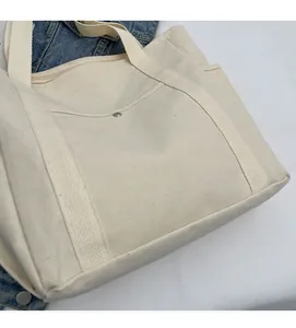 Detail of beige canvas tote bag showing top zipper closure and metal buckle front pocket