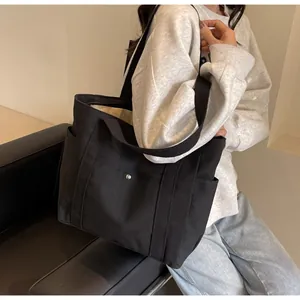 Lifestyle view of a large black canvas tote bag with side pockets on a casual model