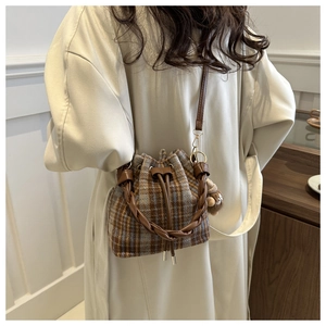 Plaid bucket bag with woven leather handle and plush charm shown on a white coat