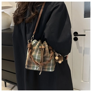 Detail of wool fabric bucket bag featuring green plaid pattern and leather drawstring