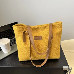 Plush yellow faux shearling tote bag with leather straps on office desk setting