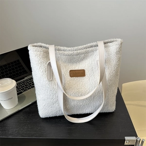 White fluffy fleece tote bag with brown leather patch on a desk with a laptop
