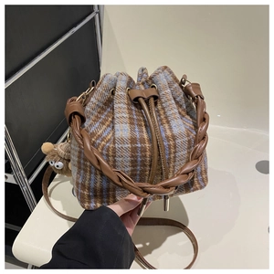 Detail of plaid bucket bag with leather woven handle and cute brown plush charm