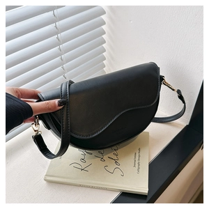 Detail of matte black PU leather saddle bag with asymmetric flap and gold hardware
