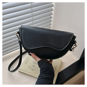 Detail of black matte saddle bag featuring wavy curved flap and gold metal hardware