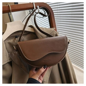 Detail of a brown leather saddle bag featuring a curved flap and slim adjustable strap