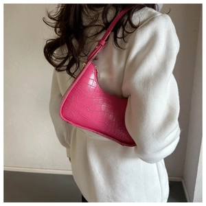 Detail of hot pink crocodile embossed baguette bag worn over a white textured coat