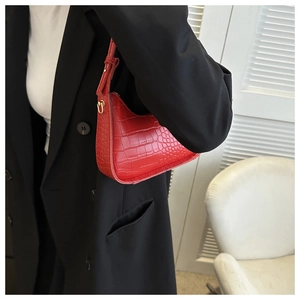 Red crocodile texture shoulder bag with gold buckle worn on a black suit blazer