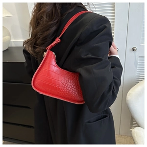 Close-up of a red crocodile pattern shoulder bag worn by a model in a modern interior
