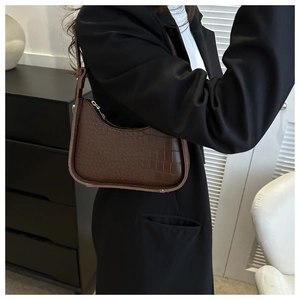 Detail of dark brown crocodile-textured underarm bag shown with a black suit for professional look