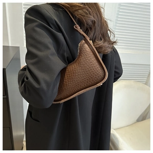 Detailed look at brown crocodile-embossed underarm bag texture on model shoulder