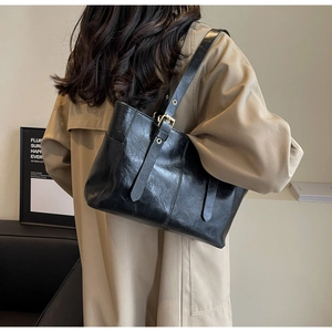 Detalle de bolso tote de cuero negro brillante con correa ajustable y ojales metálicos