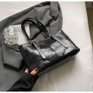 Detalle de bolso tote negro de cuero brillante con hebillas ajustables en color dorado