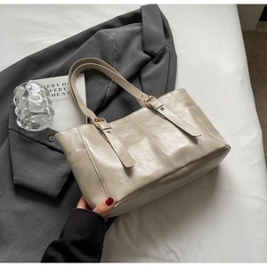 Detalle de la textura de cuero sintético beige y hebilla metálica de un bolso tote