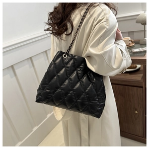 Close-up of black quilted tote bag with interwoven metal chain strap worn by a model