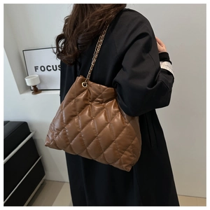 Detail shot of brown quilted crossbody bag with gold chain strap on a model's shoulder
