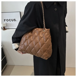 Detail view of deep brown quilted tote bag with gold chain strap on a black coat