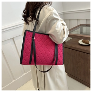 Detail of rose red quilted tote bag with black leather trim worn with a beige trench coat