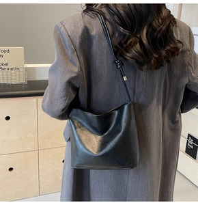 Detail showing matte black leather bucket bag with knot shoulder strap and logo embossing