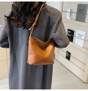 Detail of warm brown leather bucket bag with Sunday embossing and knotted shoulder strap