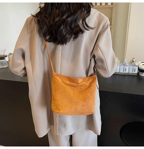 Detail of a minimalist orange suede tote bag worn by a model in a cafe setting
