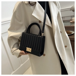 Detailed view of black quilted handbag with gold clasp on model wearing trench coat