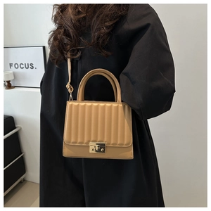 Detail of light brown pleated leather handbag with gold metal clasp on a model