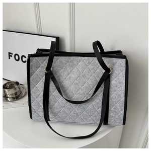 Detail of grey quilted tote bag with black leather straps and golden metal hardware