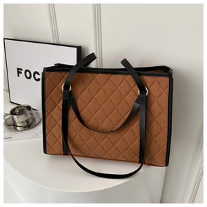 Brown quilted tote bag with diamond stitching and black leather handles in a minimal setting