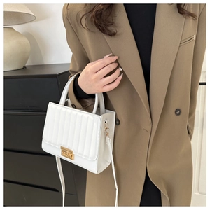 Close-up of white quilted crossbody bag with gold lock buckle and top handles